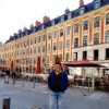 Person standing in front of historic European buildings.